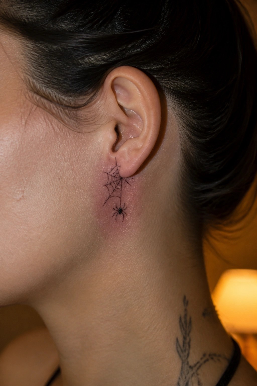 Fine line spider web tattoo placed behind the ear with the spider hanging below it in black ink.