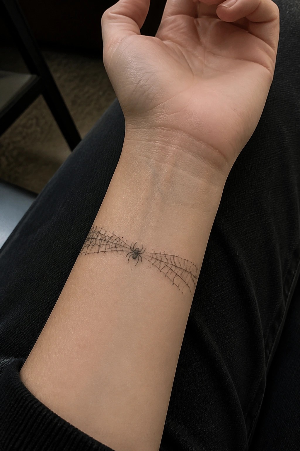 Spiderweb tattoo with spider on wrist above black sleeve