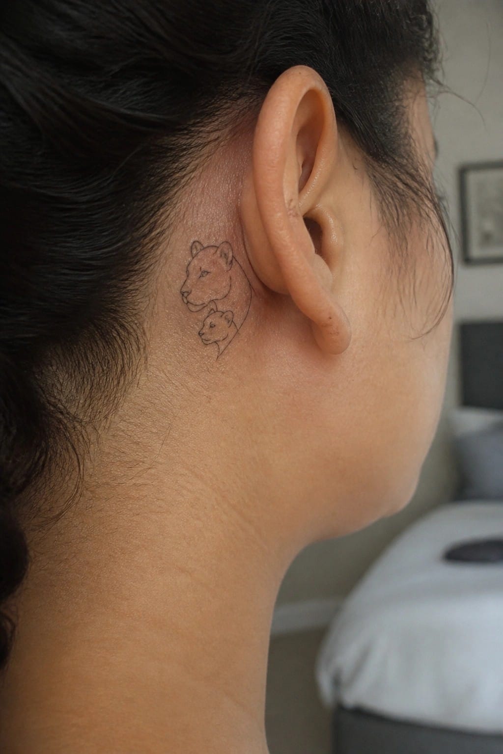 Fine line black and grey tattoo of a lioness and cub placed behind the ear on the side of the head