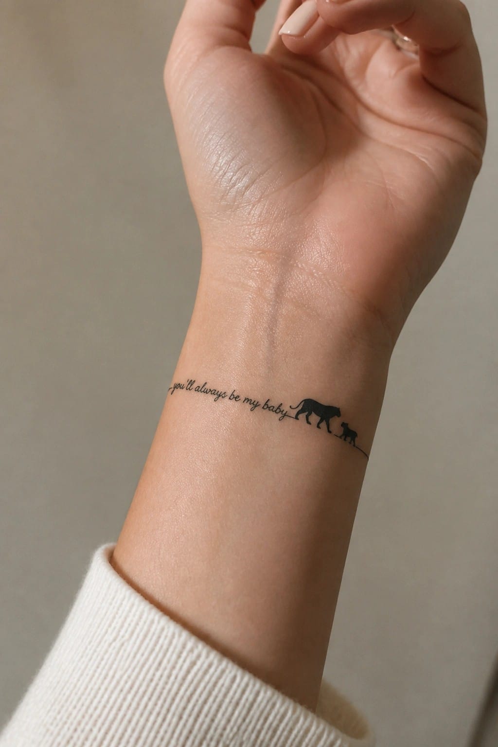 Small lioness and cub silhouette tattoo on the inner wrist with the text you'll always be my baby in script above it