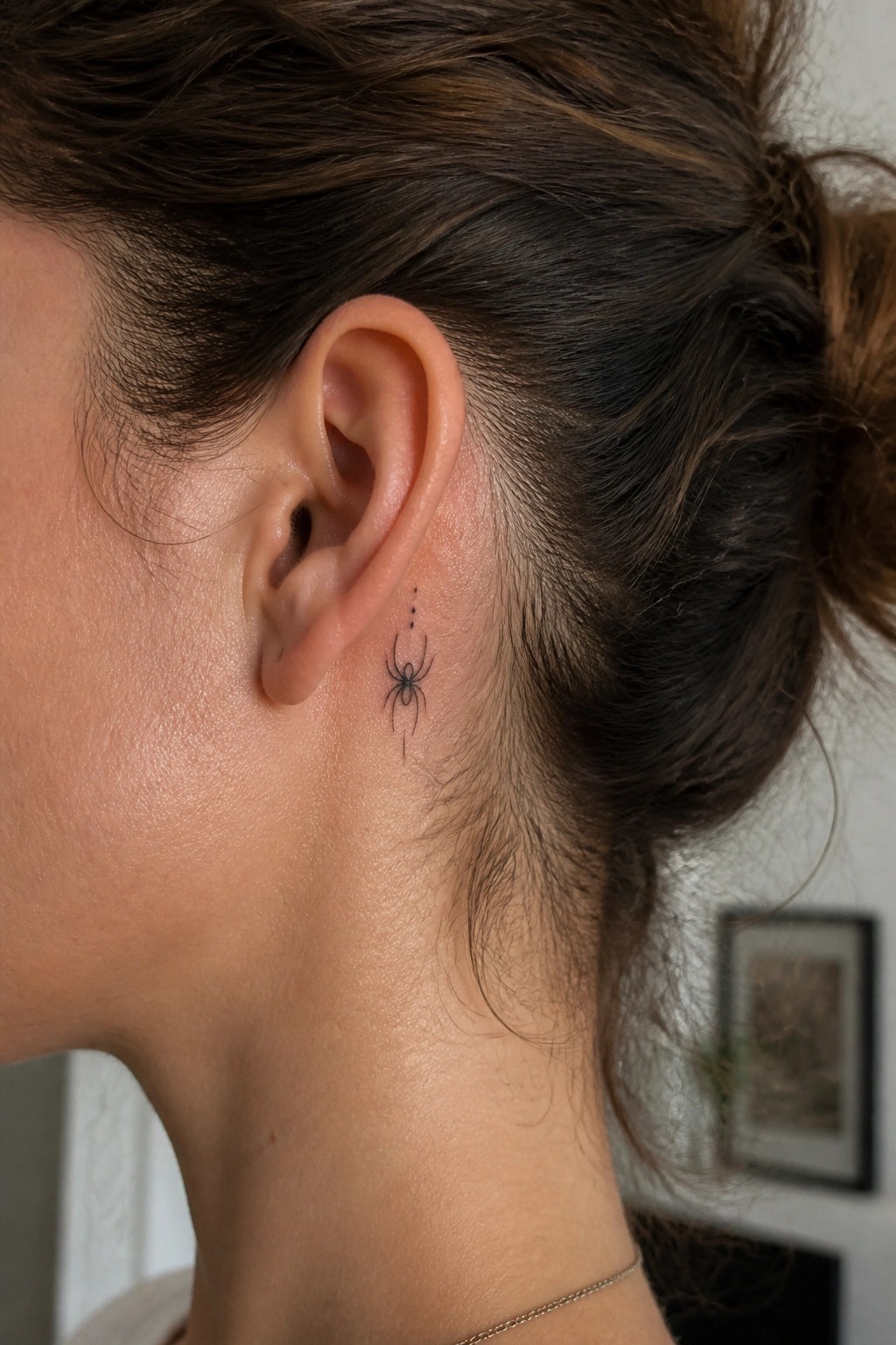 Small fine line spider tattoo with three dots above it placed directly behind a woman's ear