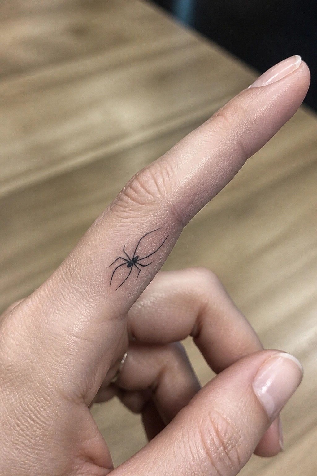 Hand with small black spider tattoo on side of index finger