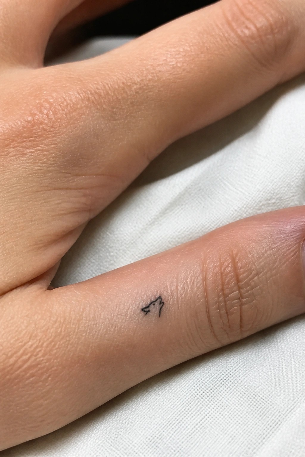 Small black line tattoo of a wolf head on the side of a finger