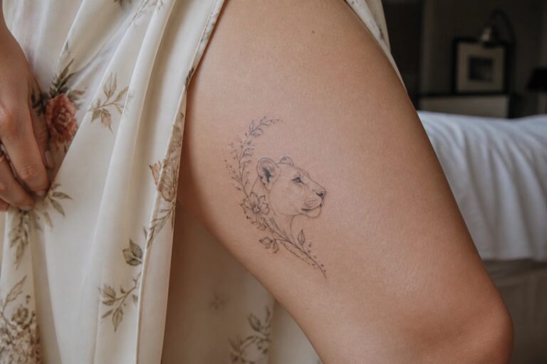 20 Flattering Lioness Thigh Tattoo Ideas That Follow Curves, Florals, and Natural Movement Lioness tattoo with floral vines on thigh under black patterned fabric