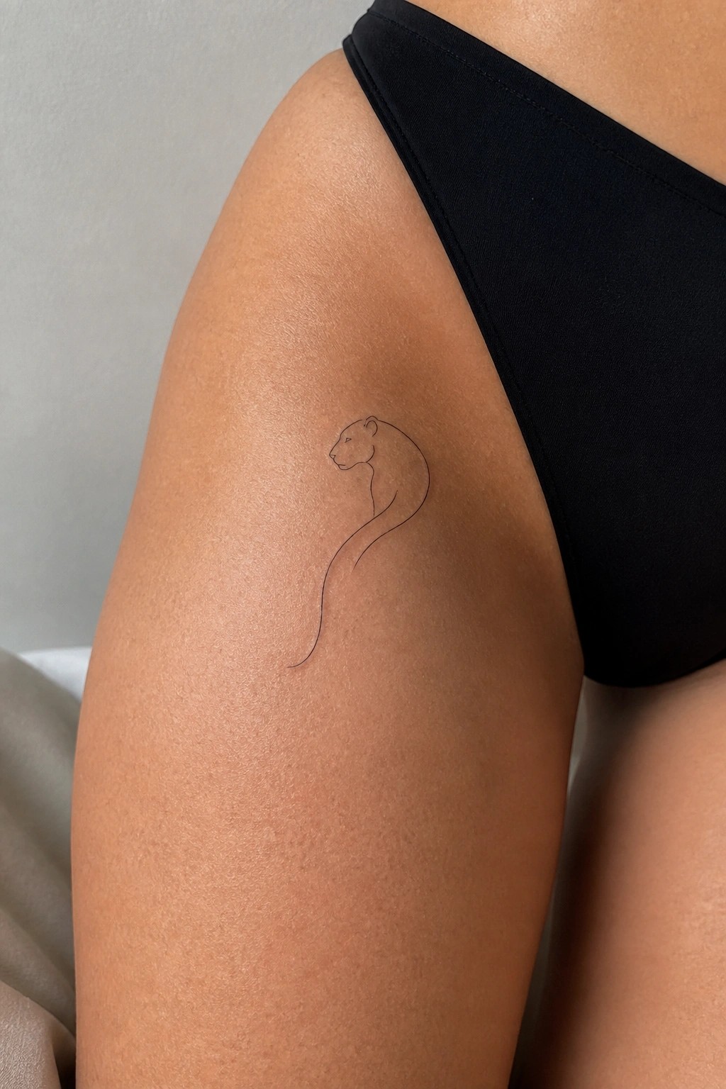 Tan thigh in black bikini with fine-line panther tattoo and long tail.
