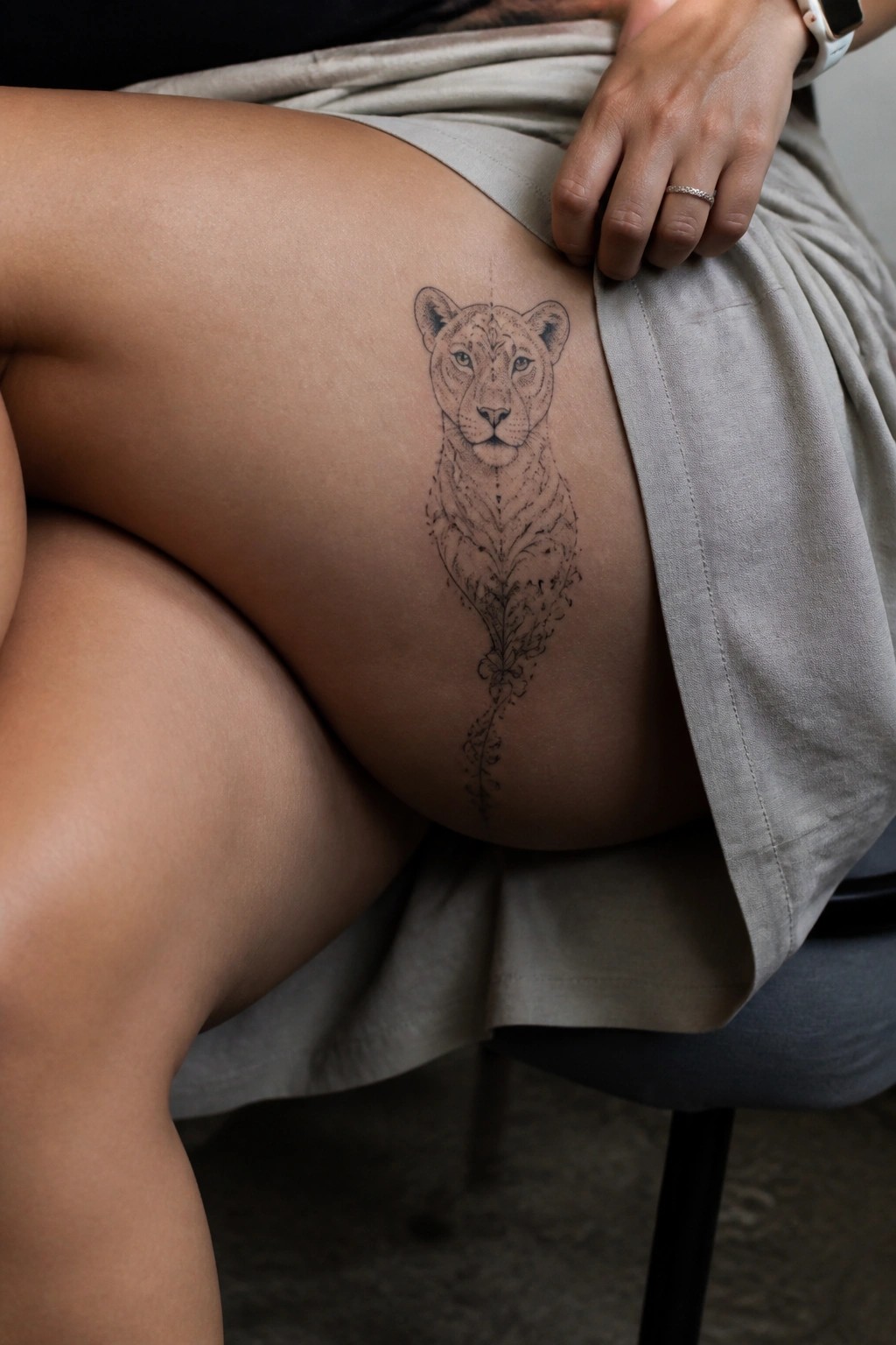Lioness tattoo on thigh with hand and ring on beige fabric skirt