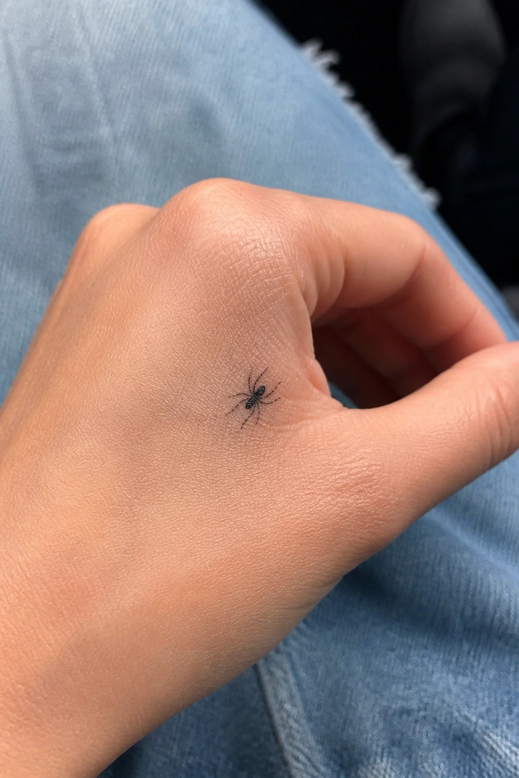 Small black spider tattoo on hand resting on blue denim jeans