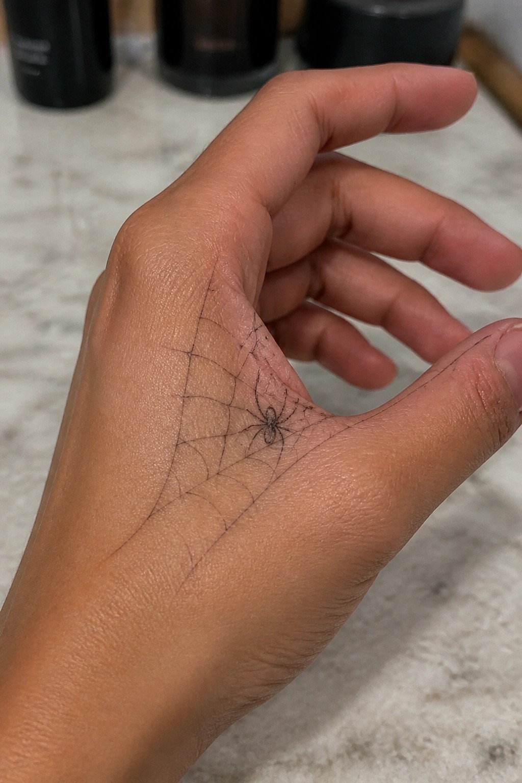 Light brown hand with black spider and spiderweb tattoo on palm