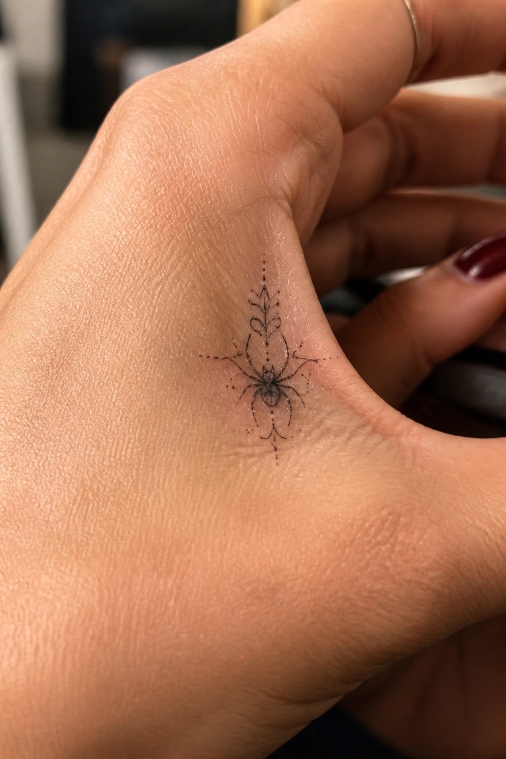 Hand with ornate black spider tattoo and dotted symmetrical patterns on palm