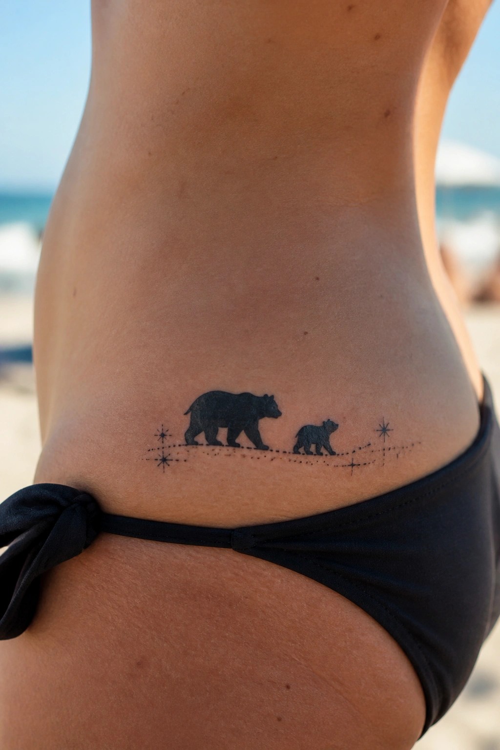 Black bear and cub tattoo above black bikini bottoms on beach skin