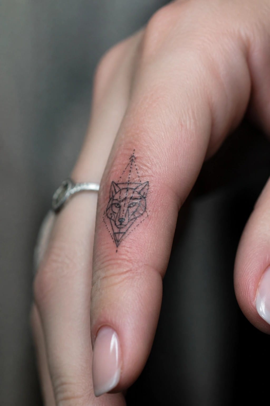 Geometric fox tattoo on finger with silver ring and pink nails