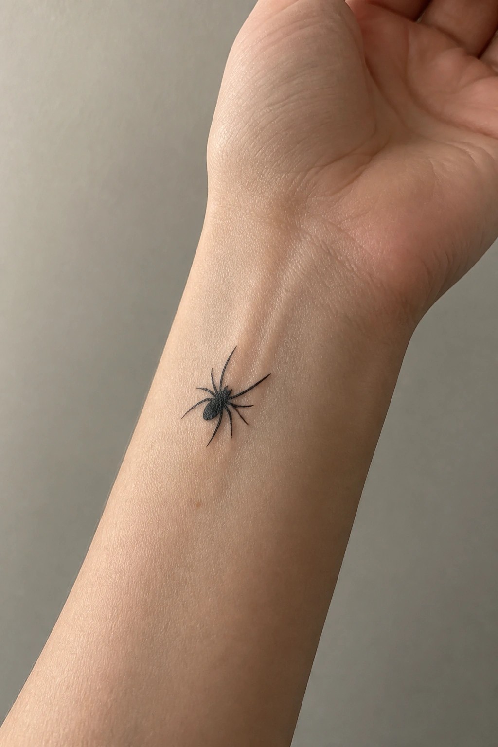 Small black spider tattoo placed on the inner wrist in minimal black ink