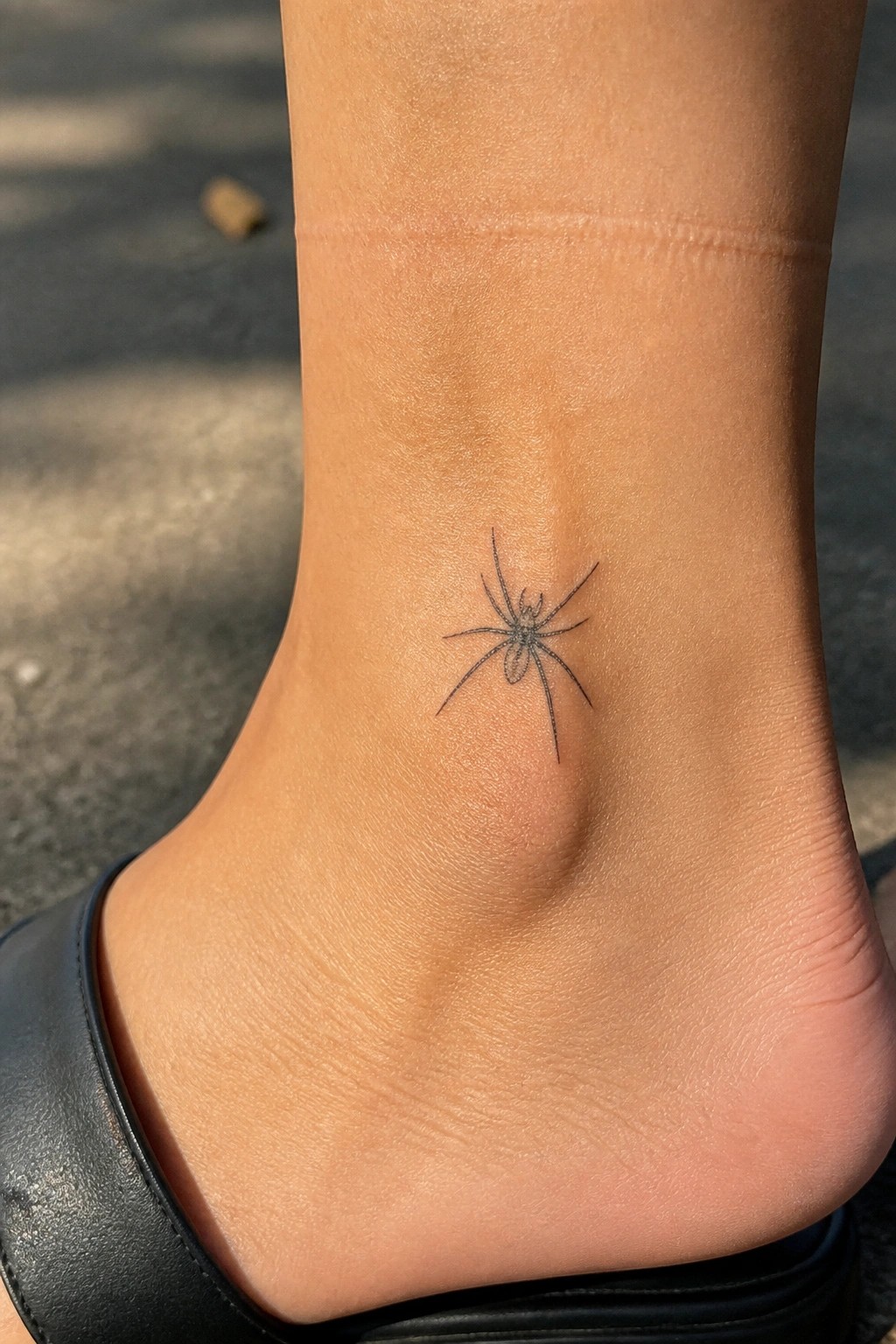 Small fine line spider tattoo placed on the side of an ankle