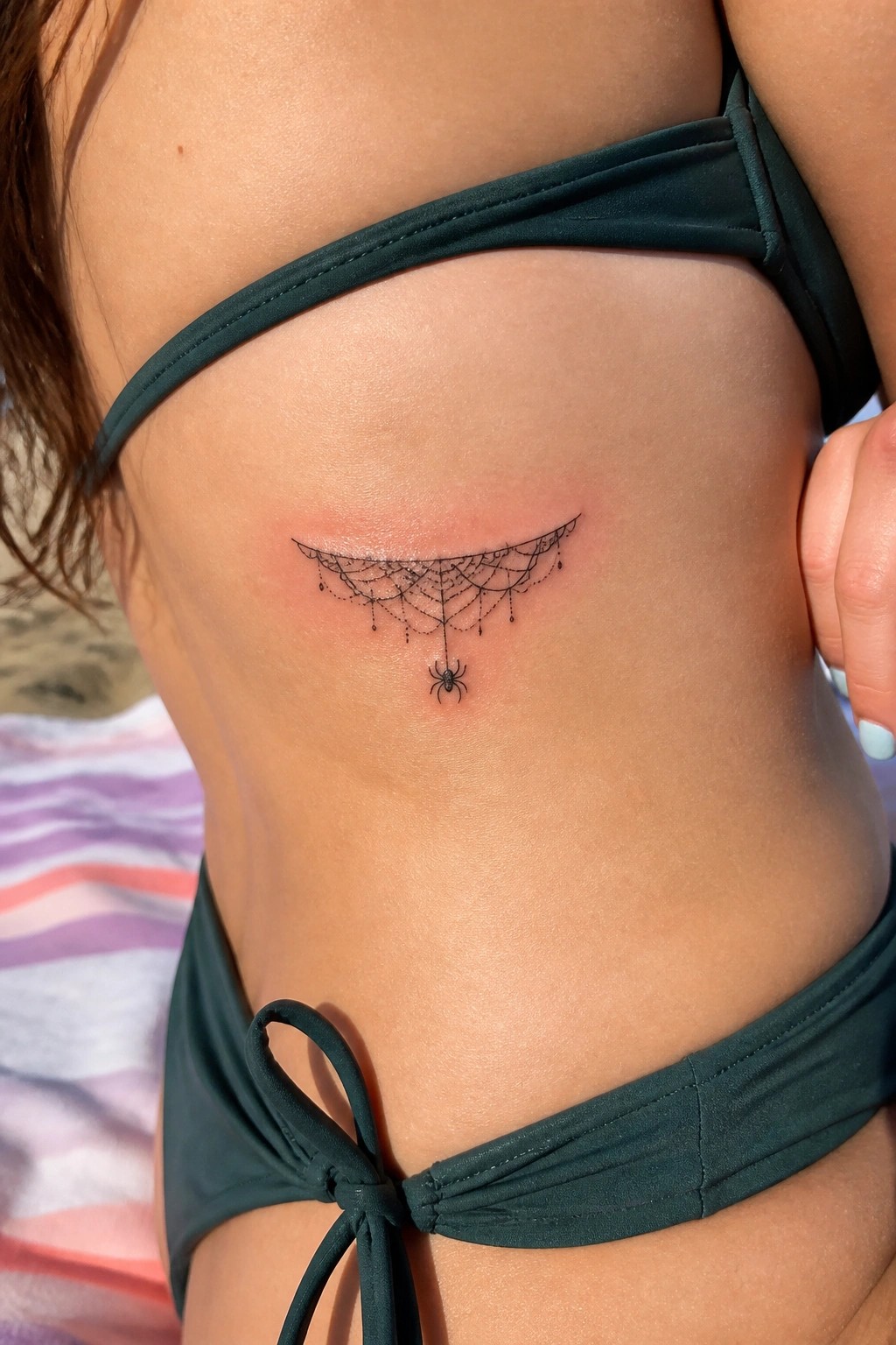 Fresh spider web tattoo with spider on reddened skin below green bikini