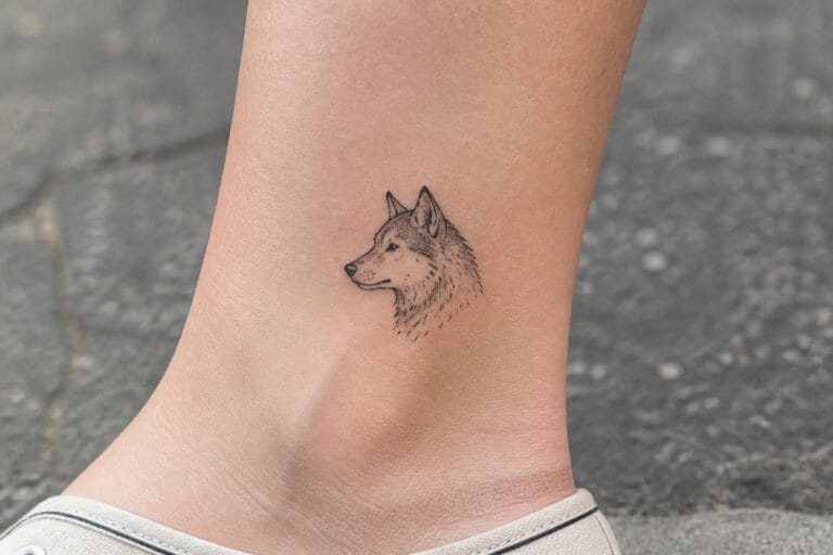 Black ink wolf head tattoo on light skin ankle above black cuff
