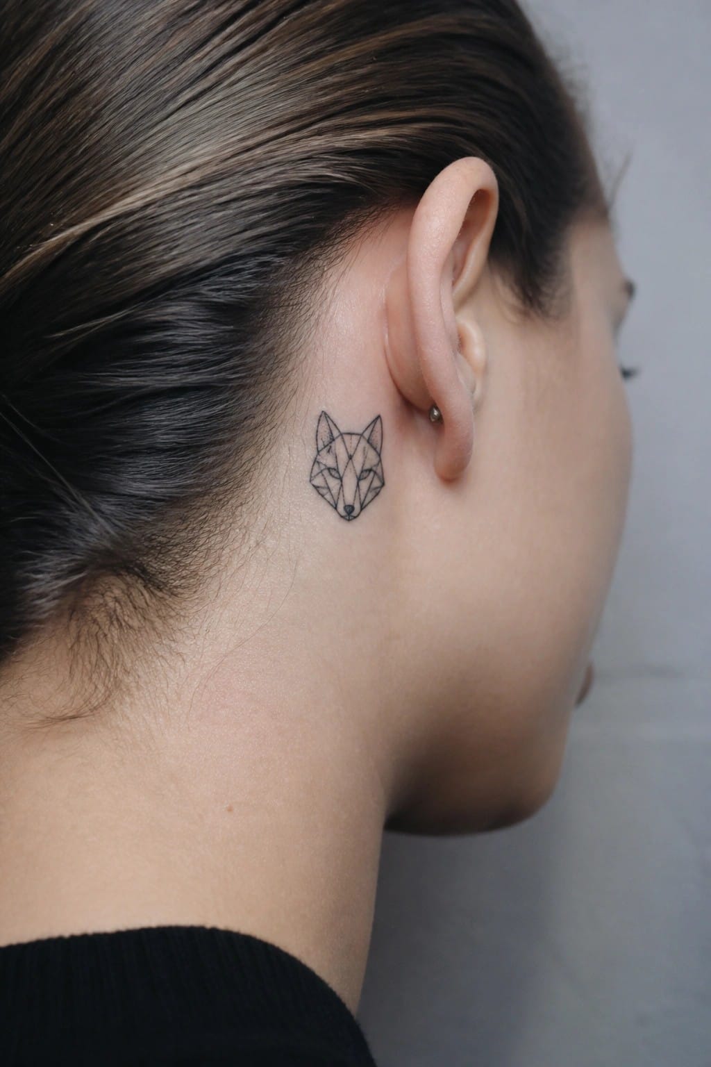 Geometric fox tattoo behind ear of person with dark pulled-back hair.