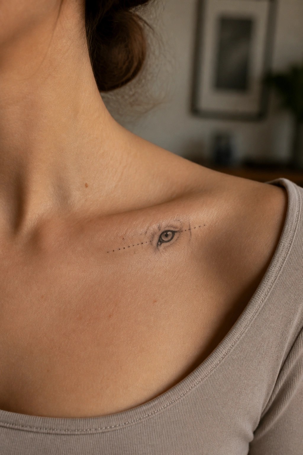 Eye tattoo with dotted lines on shoulder above beige shirt.