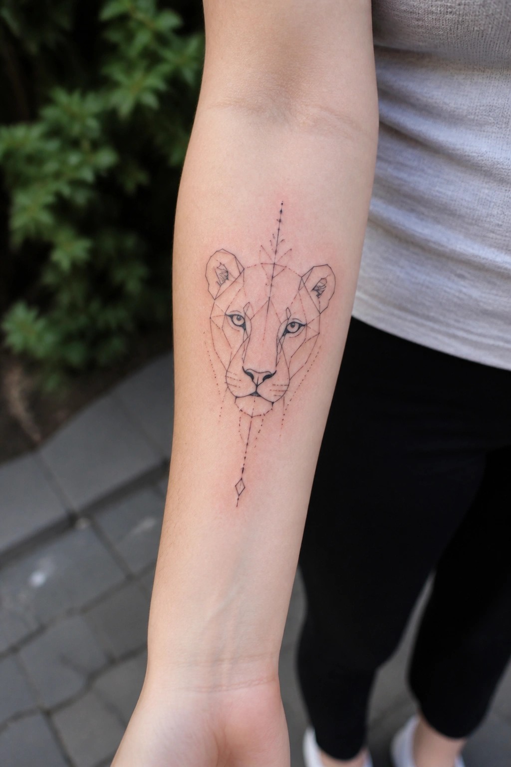 Geometric lion face tattoo on forearm with dotted lines and diamond below