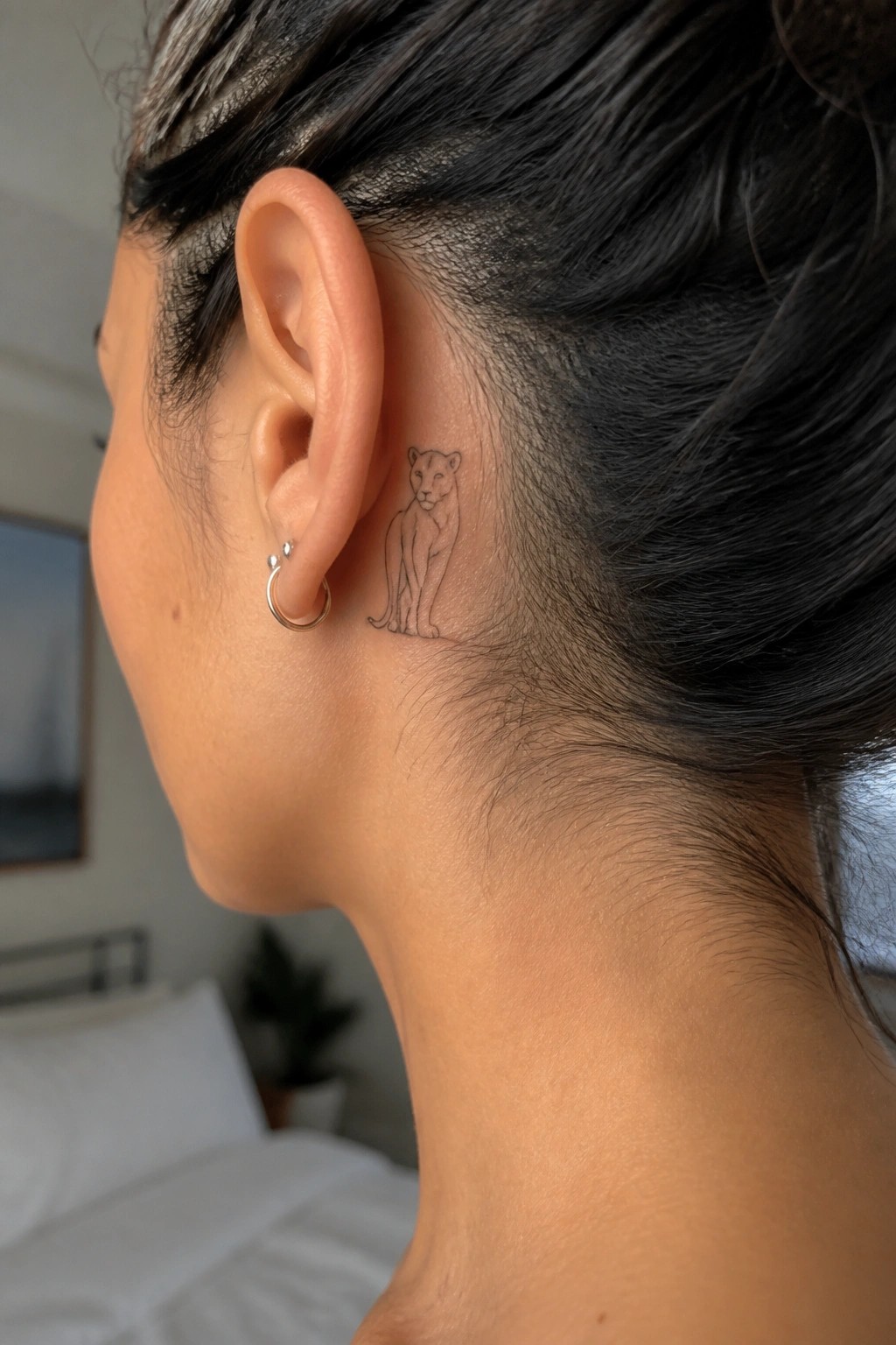 Close-up of ear with hoop earring and small feline tattoo behind it
