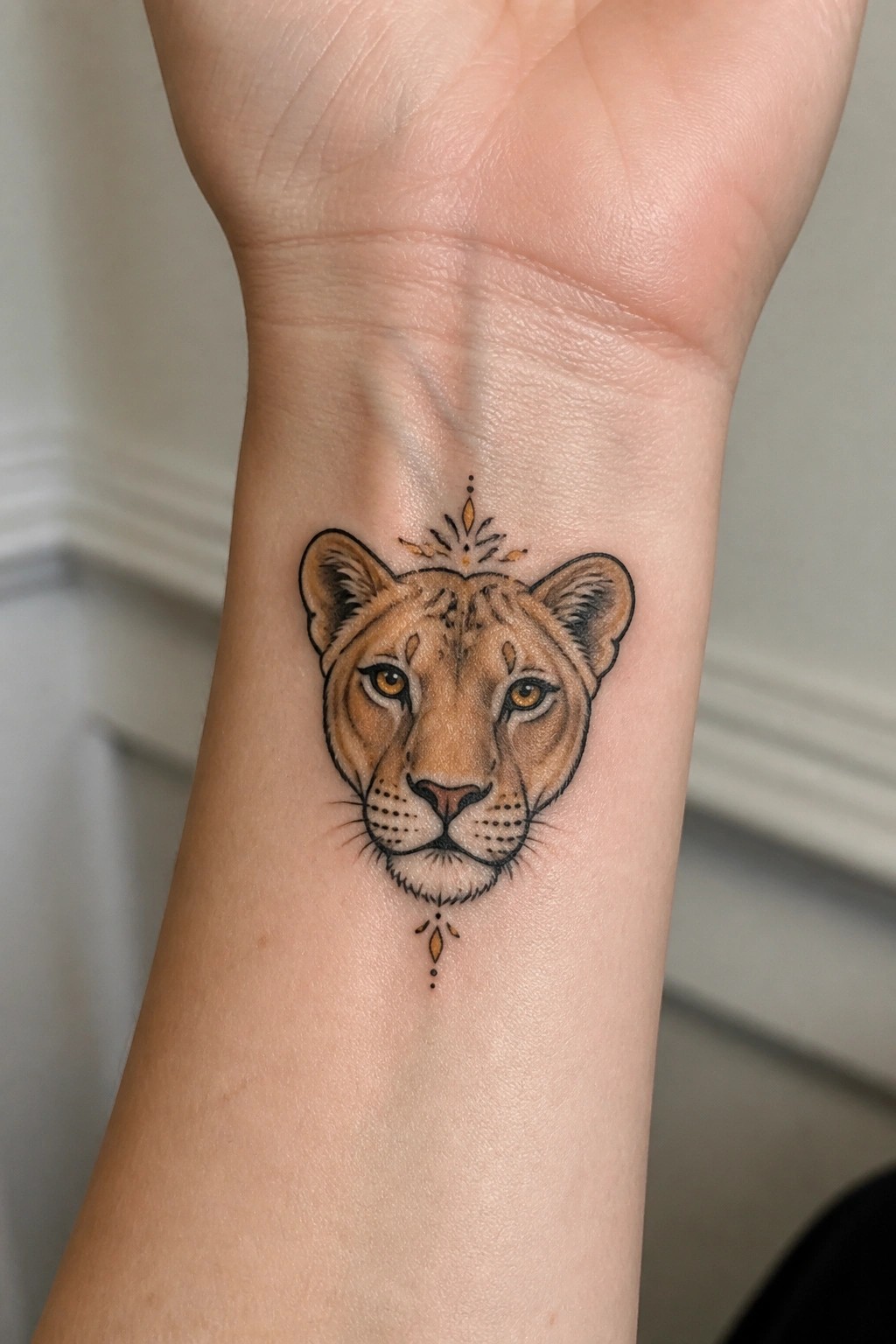 Lioness head tattoo with yellow eyes and decorative accents on wrist