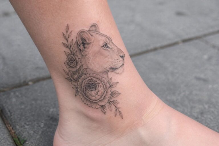 23 Graceful Lioness and Flower Tattoo Designs Featuring Roses, Peonies, and Soft Shading Fine line black and grey tattoo of a lioness head in profile with roses and peonies on the ankle.