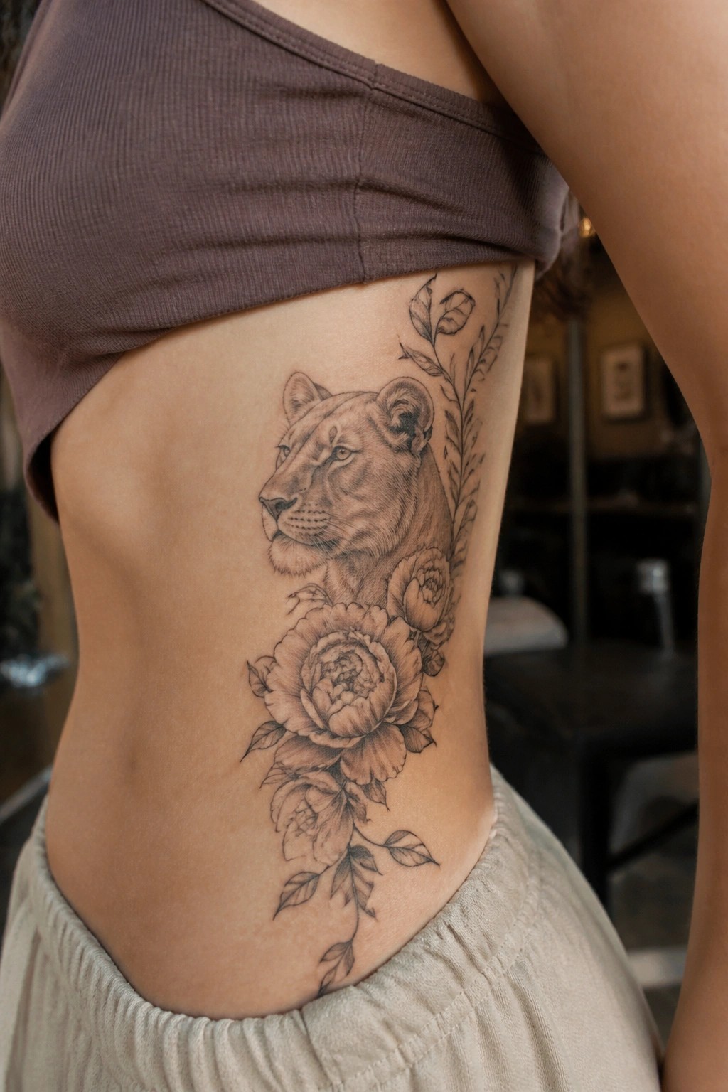 Black and grey lioness head with peonies and leaves on the side of the torso