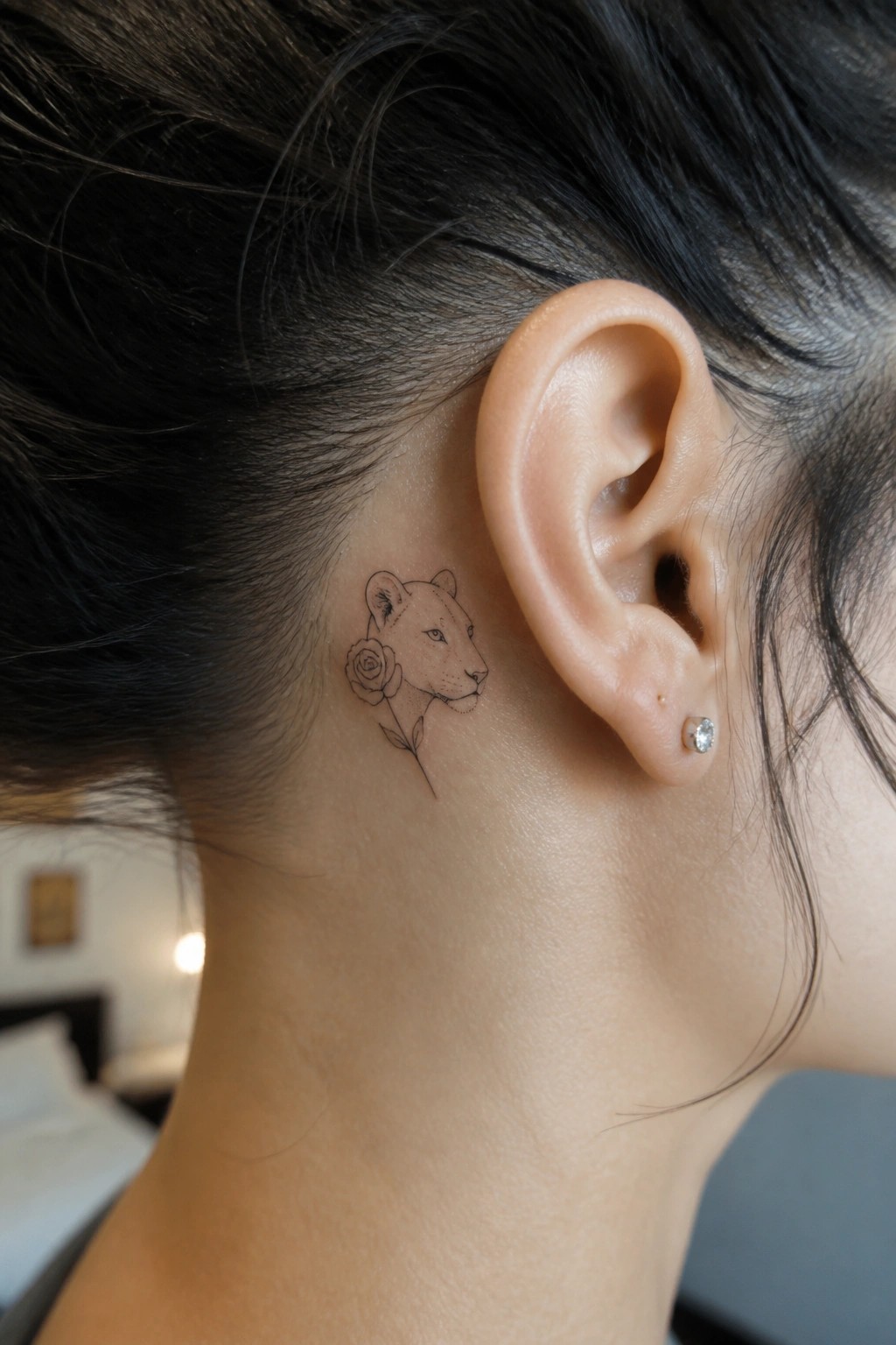 Dark hair pulled back revealing lioness rose tattoo behind ear with stud.