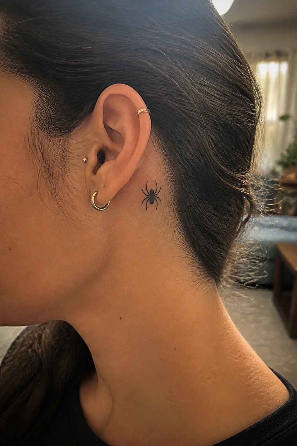 Side view of ear with gold piercings and black spider tattoo behind it.