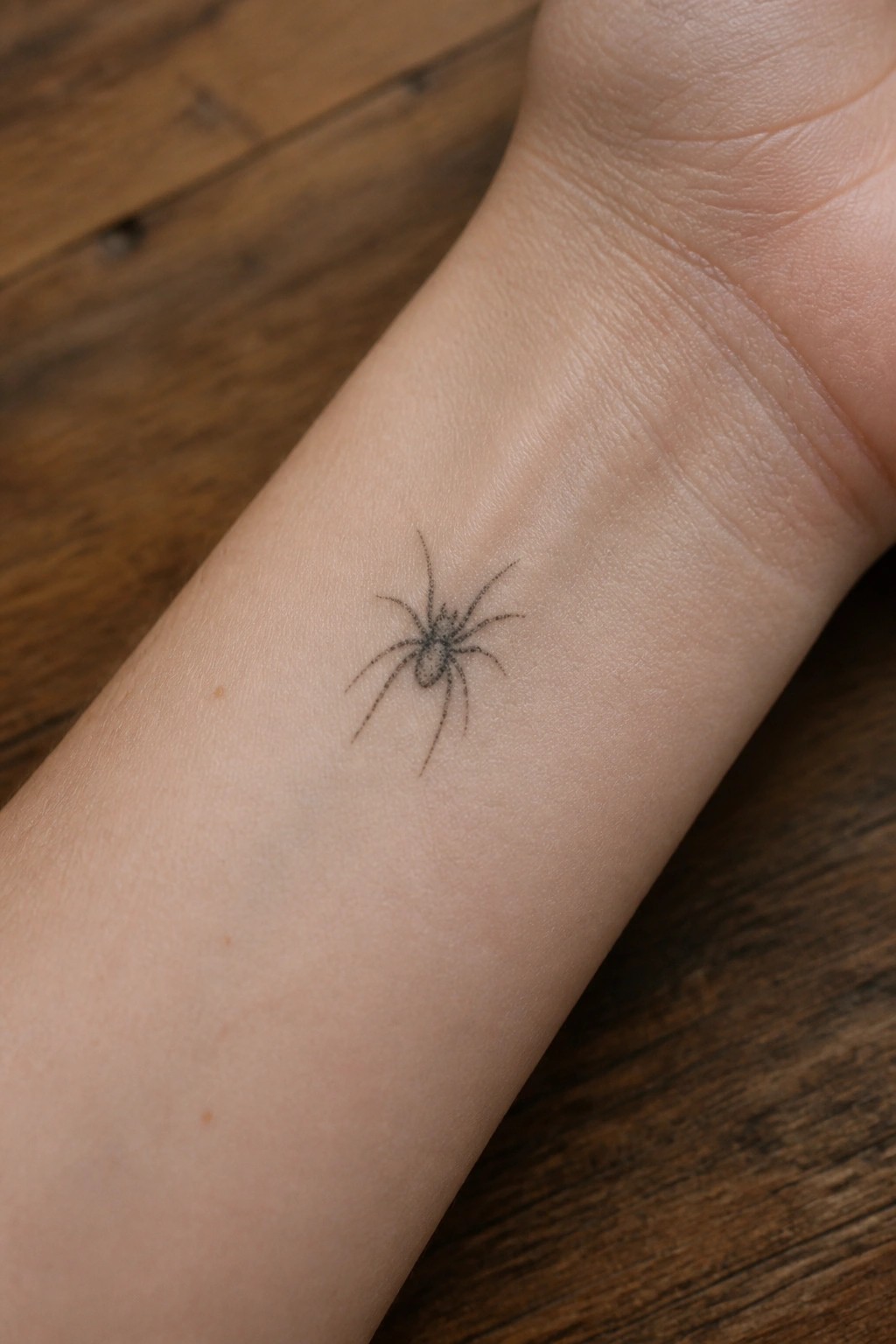 Small fine line spider tattoo on the inner wrist.