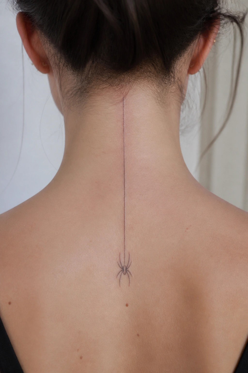 Dark hair in bun above vertical line tattoo ending in spider on back