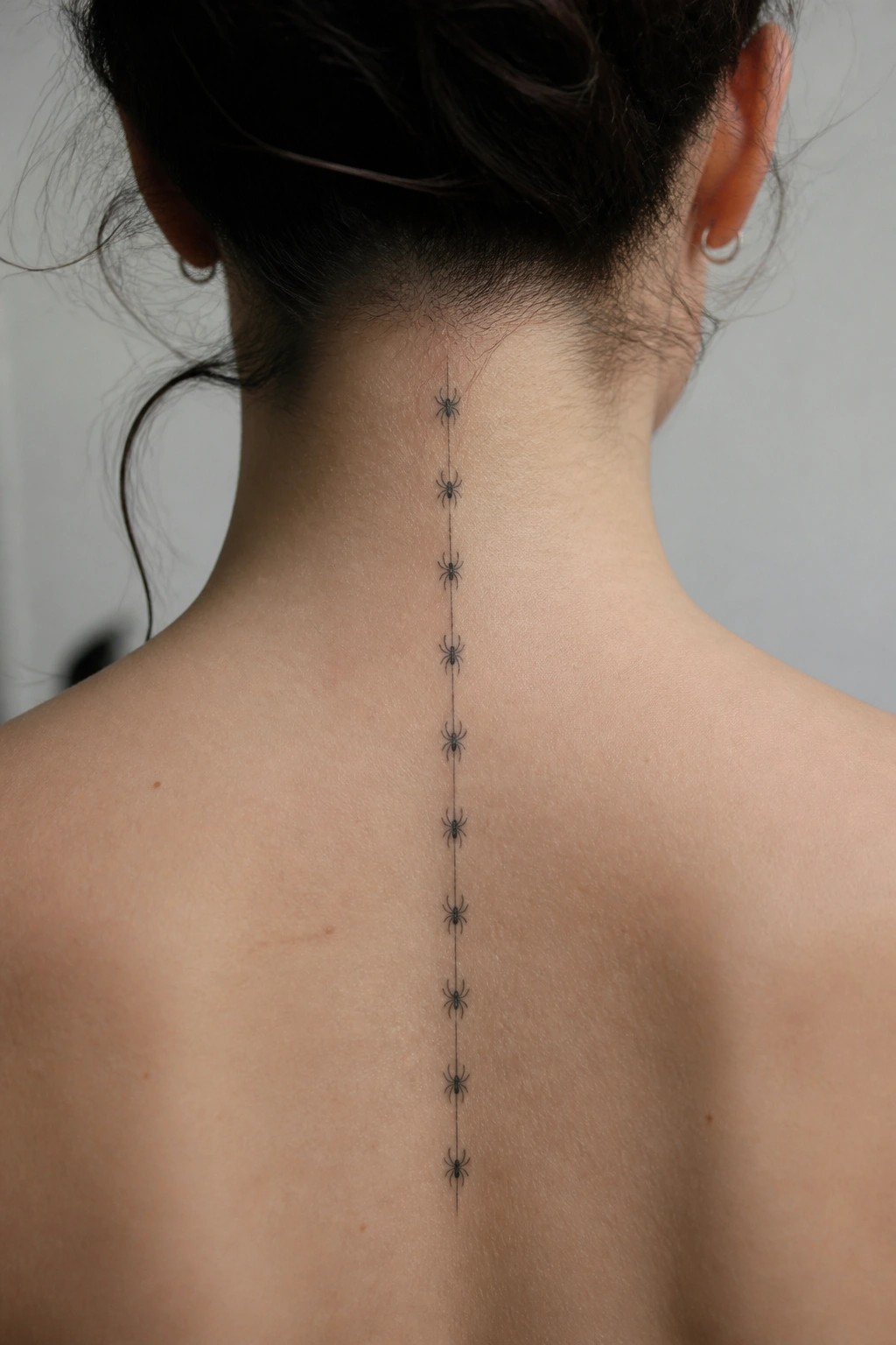 Small black spiders connected by a thin vertical line tattooed down the center of a woman's spine.