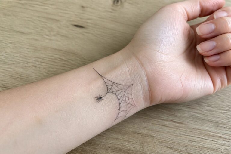 Fine line spider web tattoo with a hanging spider on the inner wrist