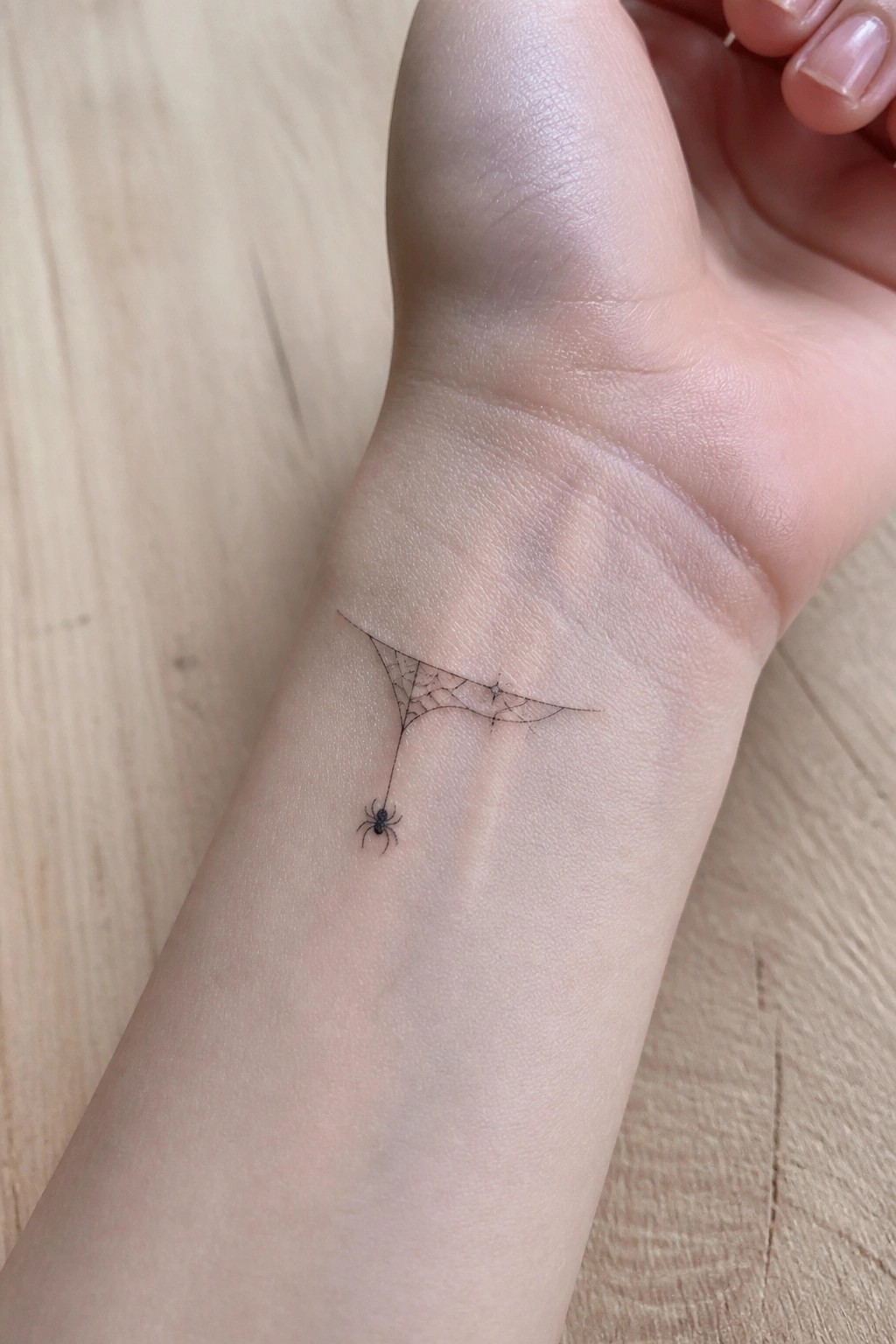 Fine line spider web tattoo with a hanging spider on the inner wrist