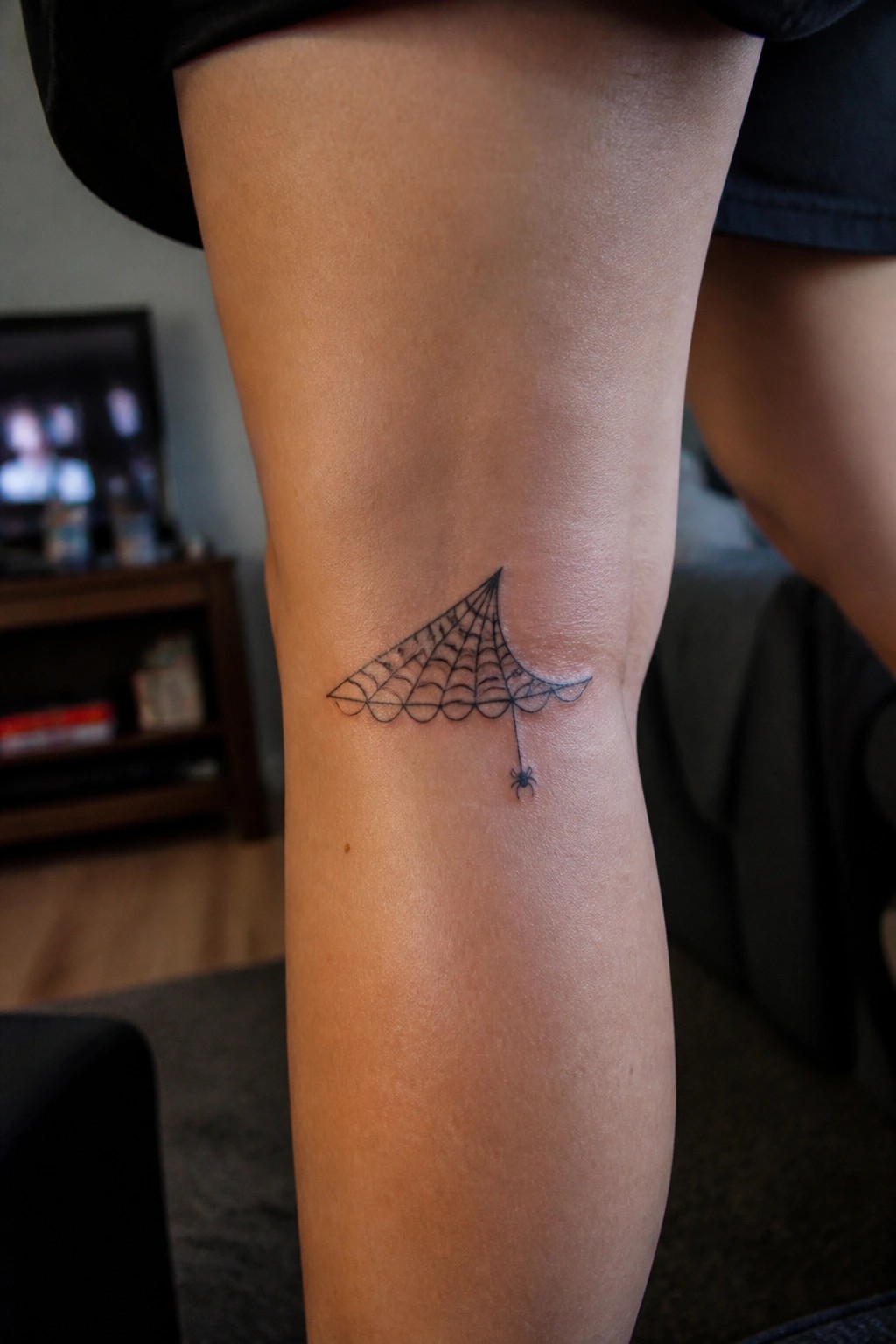 Black spiderweb tattoo with dangling spider on leg in black shorts
