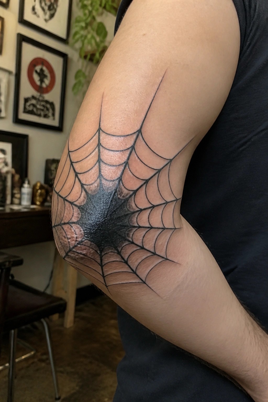 Black spiderweb tattoo wrapping around elbow on arm in black shirt