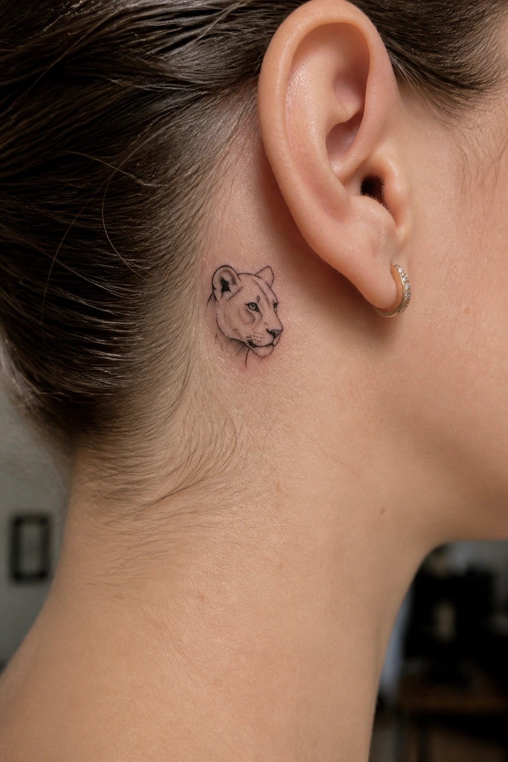 Small fine line lioness head tattoo placed behind the ear on the side of a woman's head
