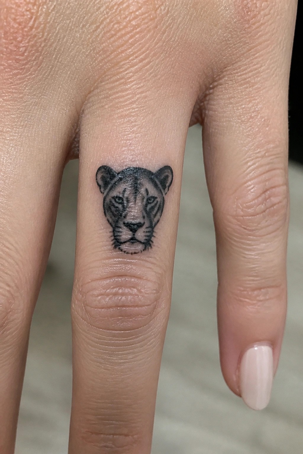 Small blackwork lioness head tattoo on the side of a finger above the knuckle.