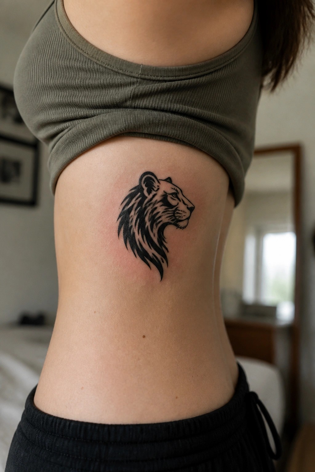 Lion tattoo on side of torso below olive green crop top and black waistband.
