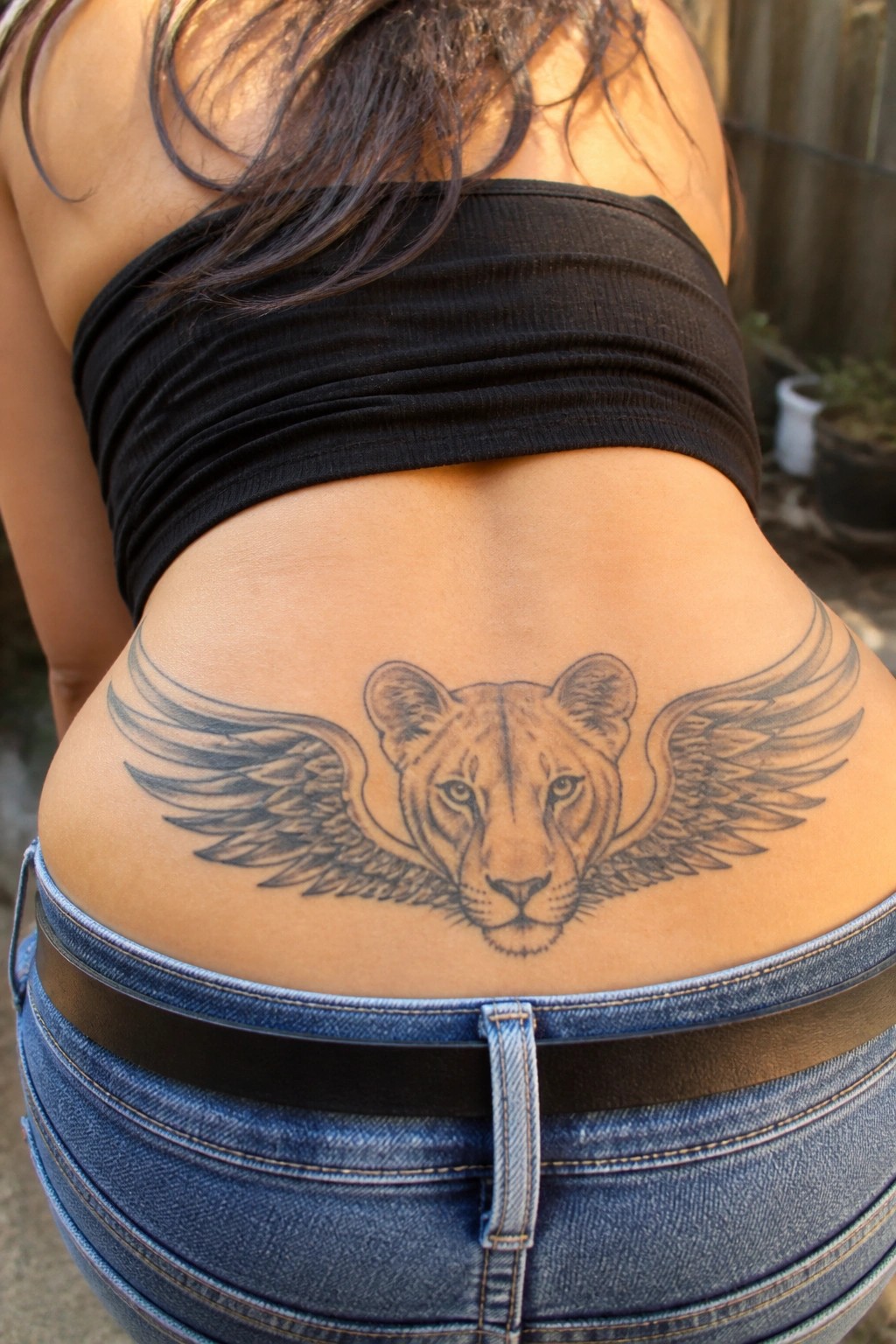 Blackwork tattoo of a winged lioness centered on the lower back above denim jeans.