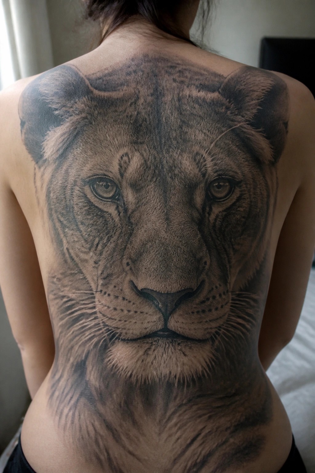 Large realistic black-and-gray lion face tattoo covering a bare back