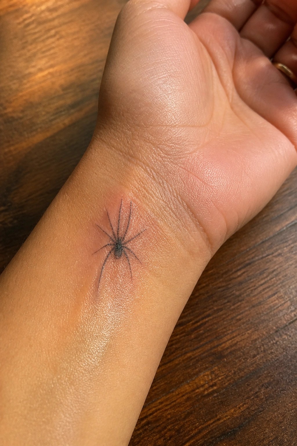 Fine line spider tattoo on the inner wrist showing thin detailed legs in a small realistic style.