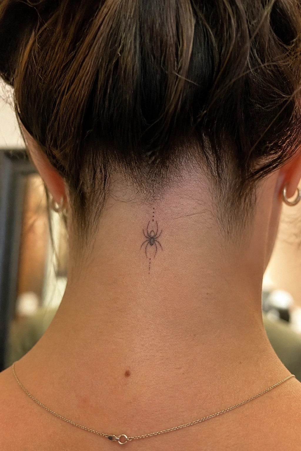 Fine line spider tattoo with dotted lines centered on the back of the neck below the hairline