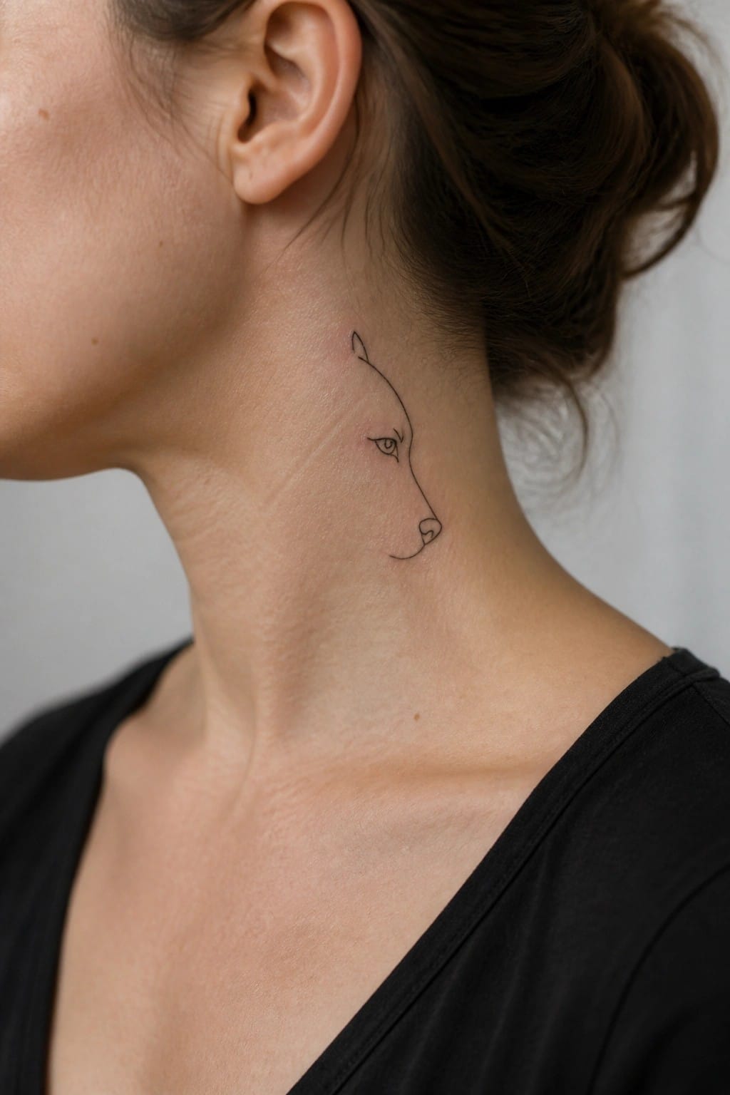 Minimalist black line wolf tattoo on a woman's neck with dark hair in a bun