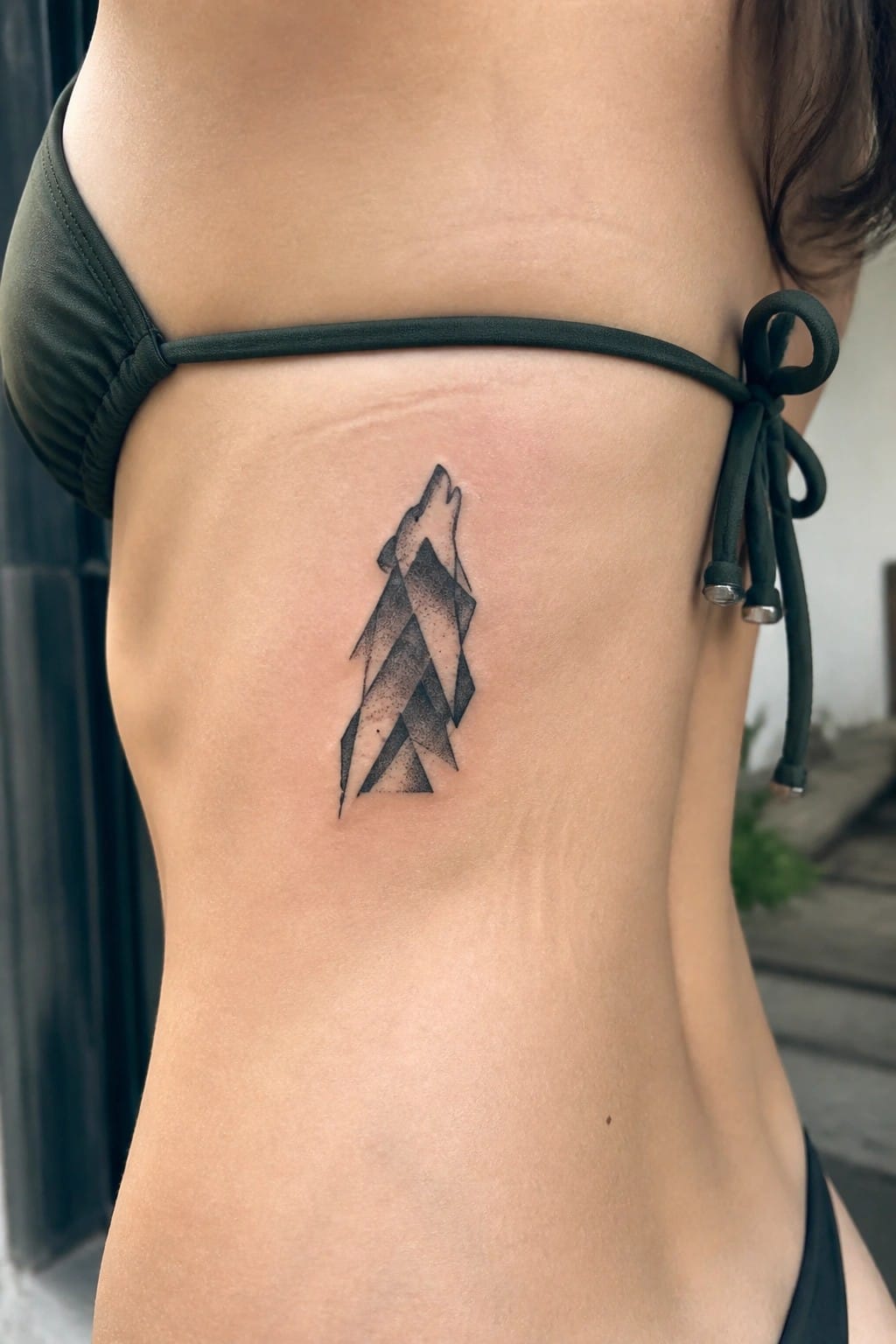 Minimalist geometric wolf tattoo on the side torso in black ink with triangle shapes and dot shading
