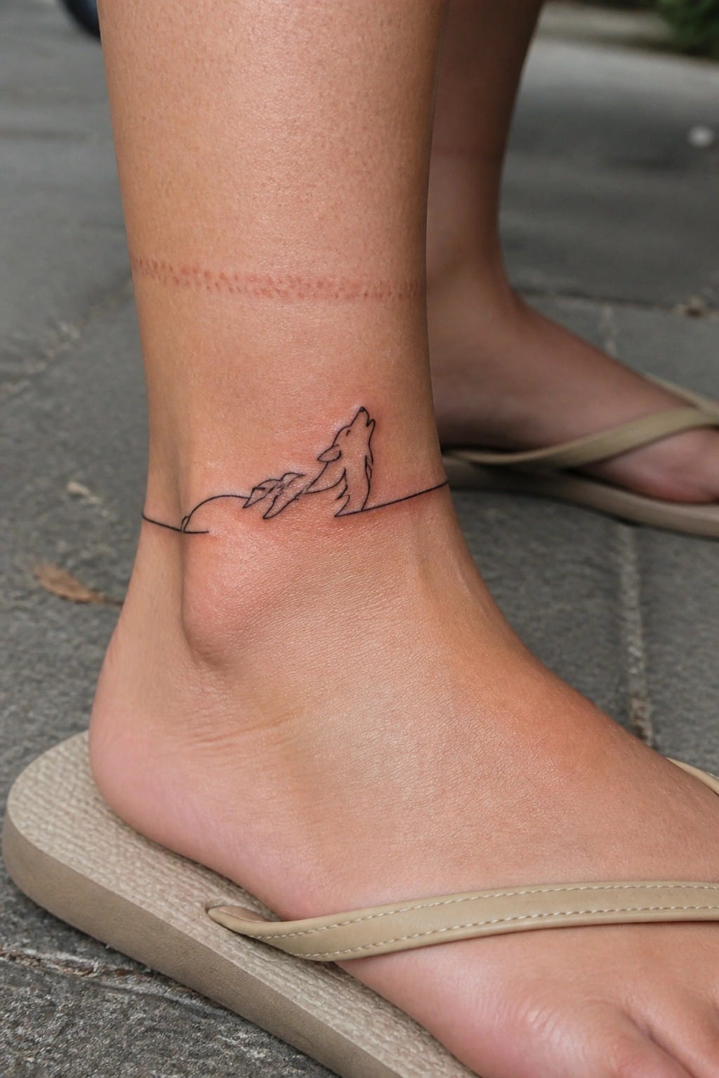 Ankle with black howling wolf line tattoo, red scar above, in beige flip-flop.