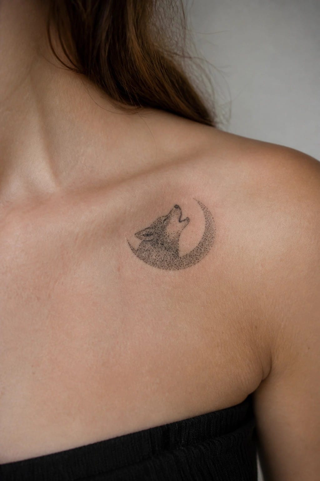 Shoulder with black dotted tattoo of howling wolf and crescent moon above black top