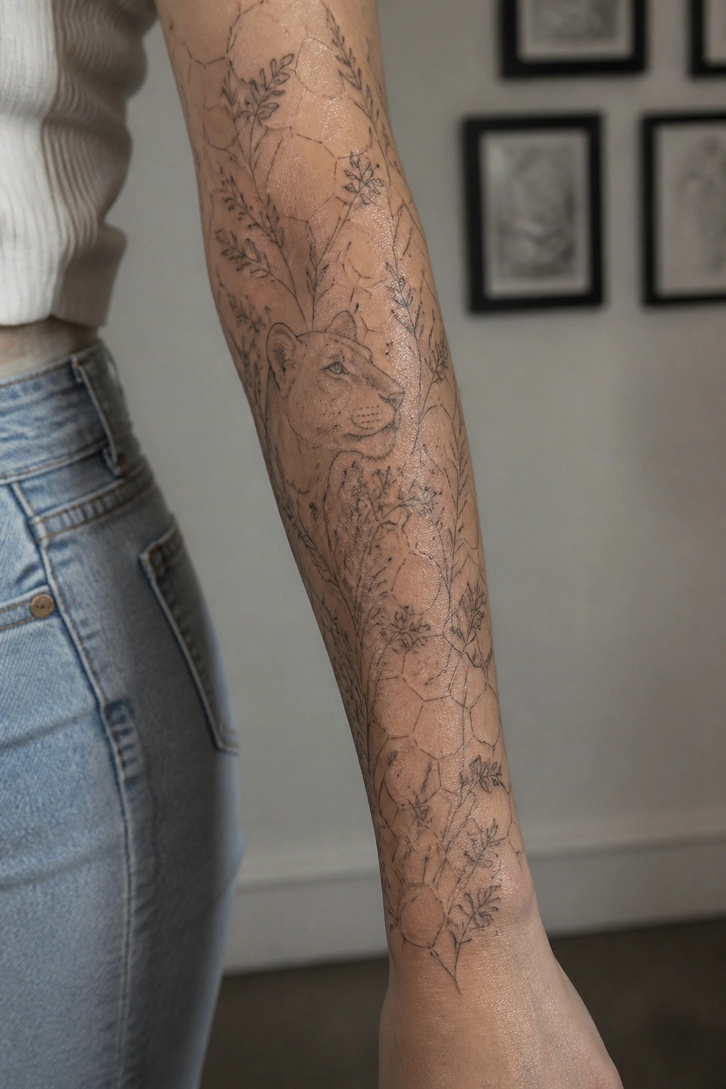 Black line tattoo of a lioness head on an arm with surrounding leaves and geometric patterns covering the sleeve area.