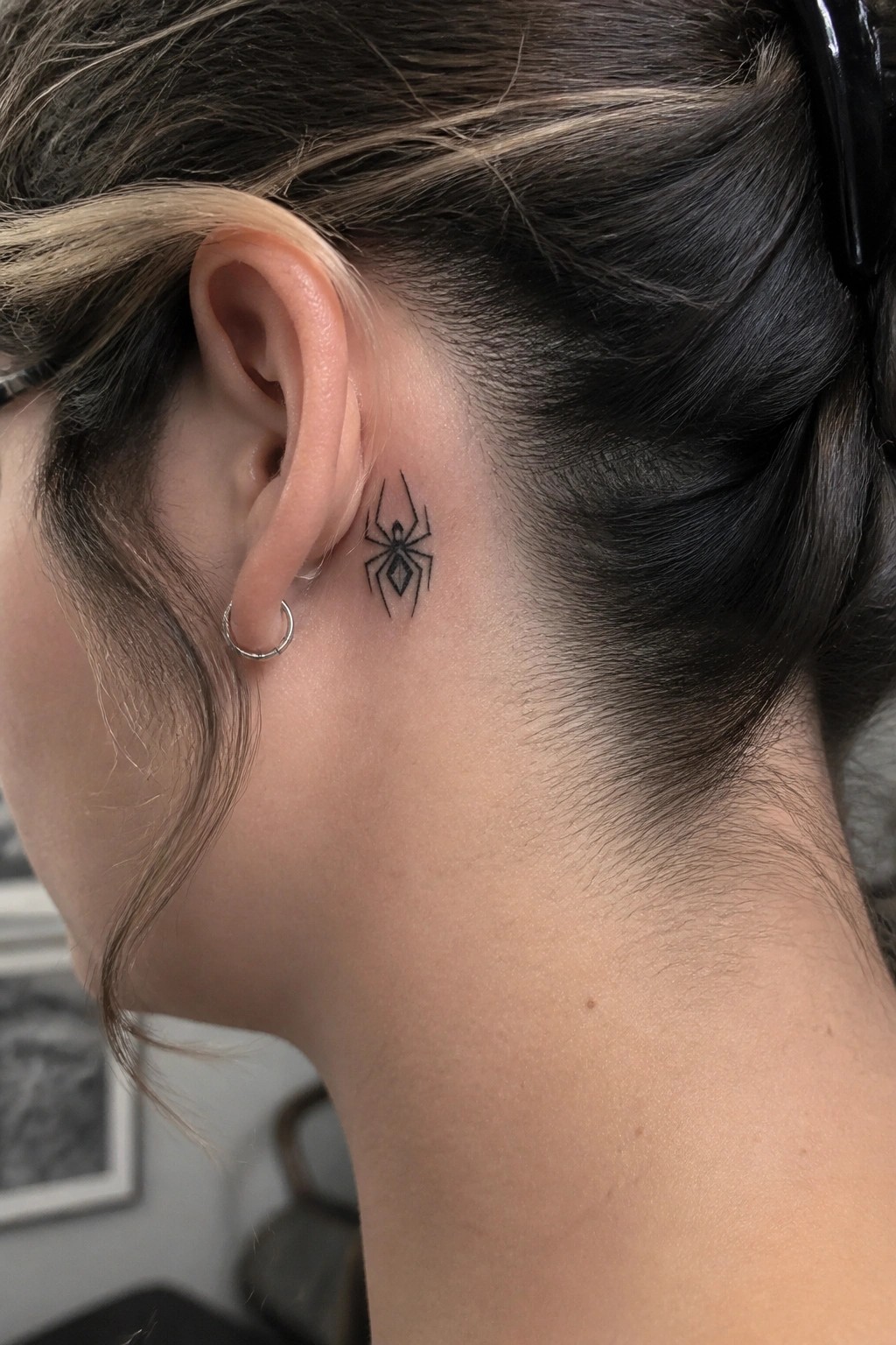 Black spider tattoo behind ear on neck, dark hair pulled back.