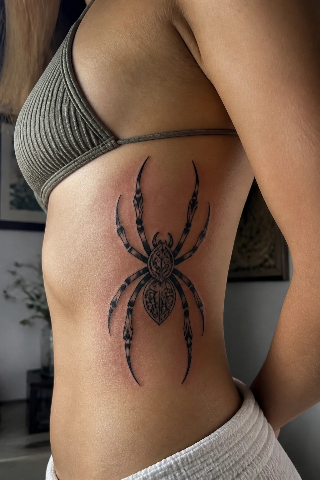 Blackwork spider tattoo on the side torso showing detailed body patterns and extended legs in high contrast ink.