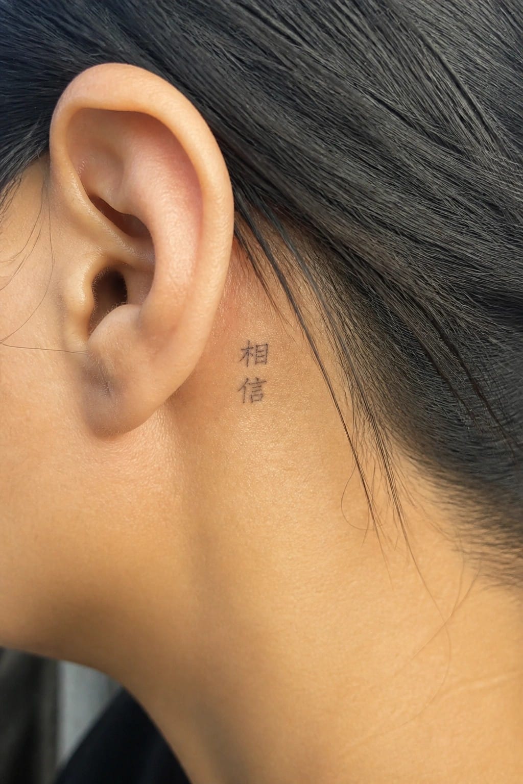 Small Chinese characters tattooed behind a woman's ear in black ink